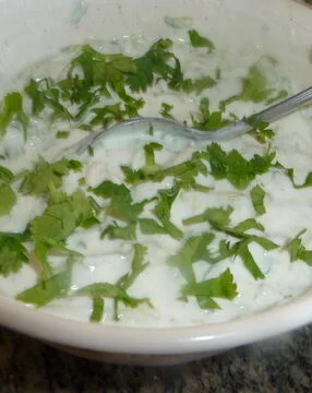 A bowl of food with greens and yogurt.