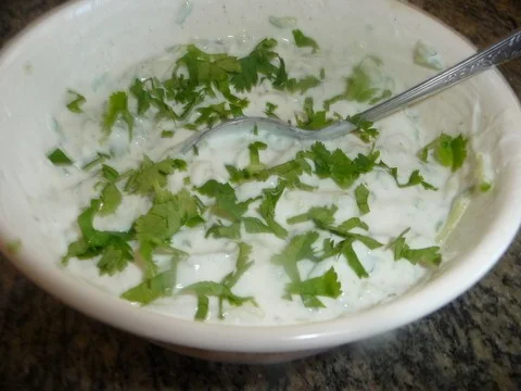 A bowl of food with greens and yogurt.