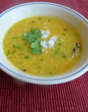 A bowl of soup with cilantro on the side.