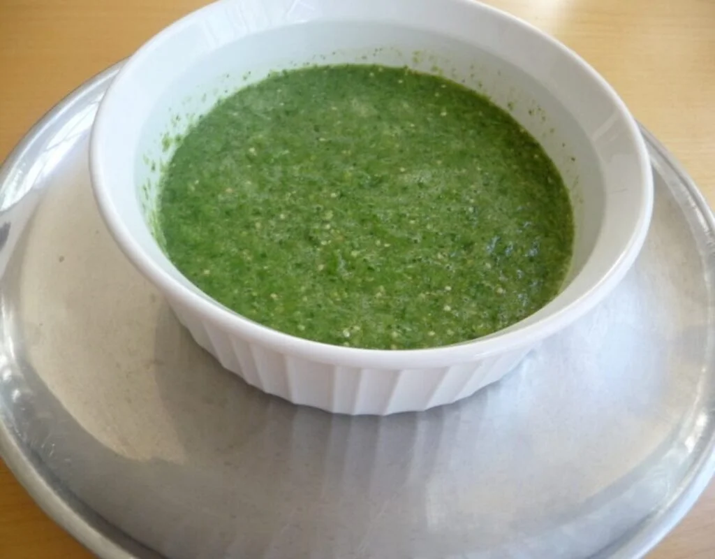 A bowl of green sauce on top of a table.