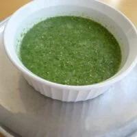 A bowl of green sauce on top of a table.