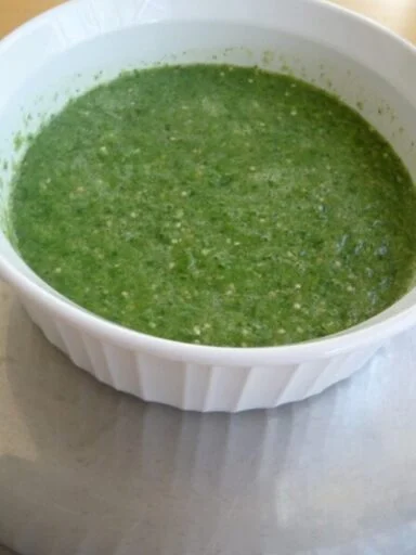 A bowl of green sauce on top of a table.