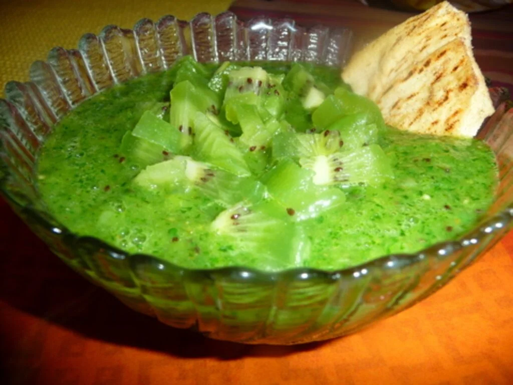 A bowl of green food with crackers on the side.