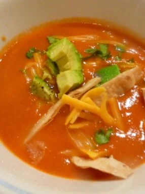 A bowl of soup with tortilla strips and avocado.