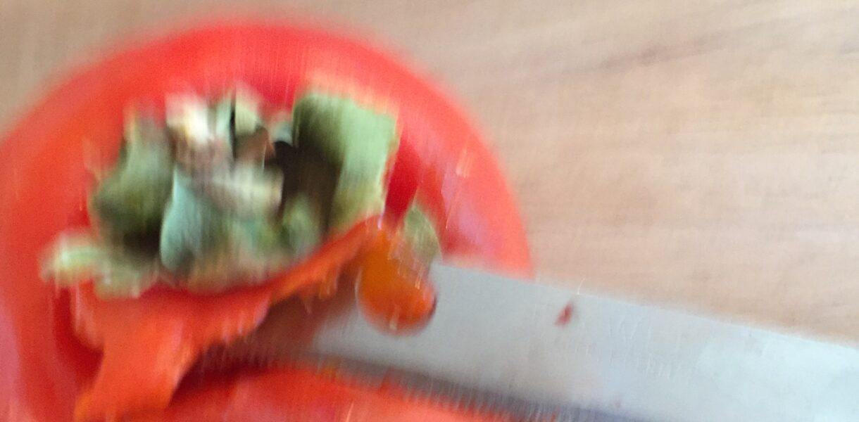 A tomato being cut with a knife.